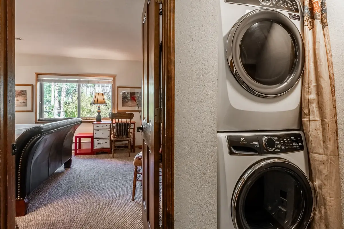 Stacked Electrolux washer and dryer in a hall nook beside an open door to a bedroom with a desk and window