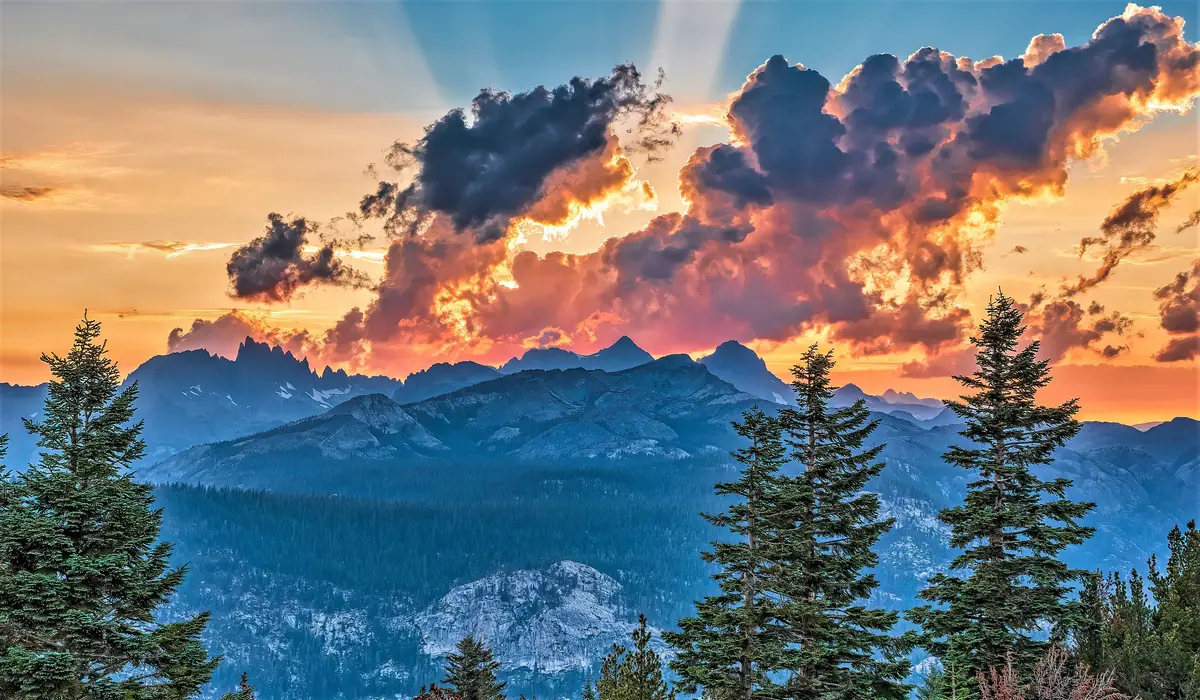 Fiery orange sunset clouds and sunbeams over the blue silhouette of the Ritter Range and Volcanic Ridge, seen from Minaret Vista