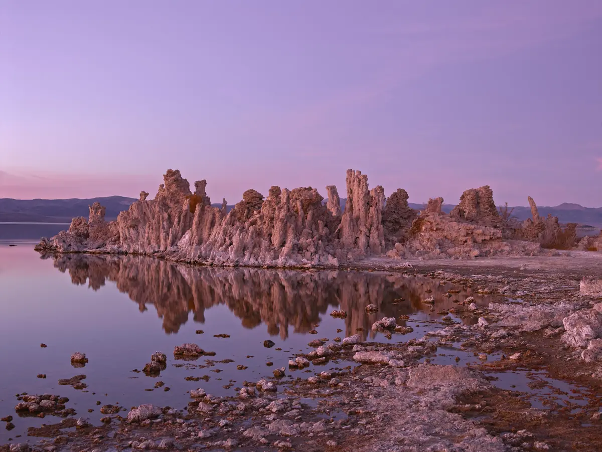 Tufa towers at Mono Lake glowing pink at dawn and mirrored in the still water under a lavender sky