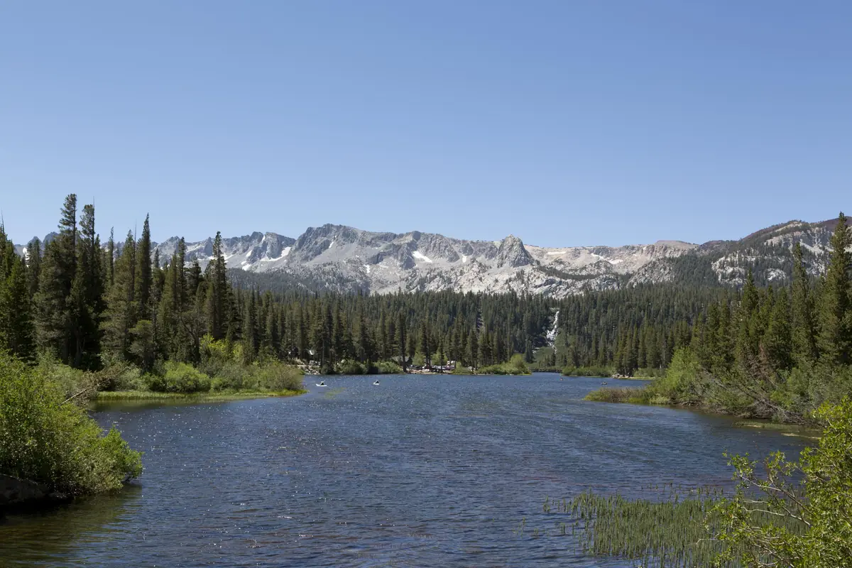Twin Lakes in summer with kayakers on the blue water, pine forest, Twin Falls spilling down the slope and the granite Mammoth Crest beyond
